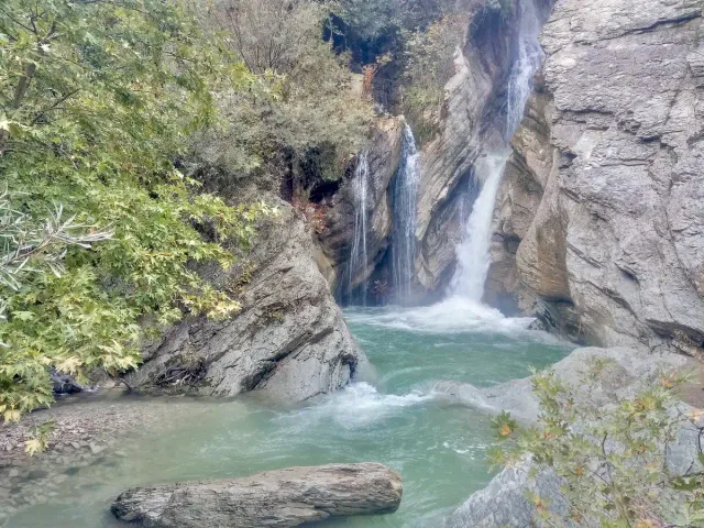A white waterfall dropping between rock walls into a shallow forest stream