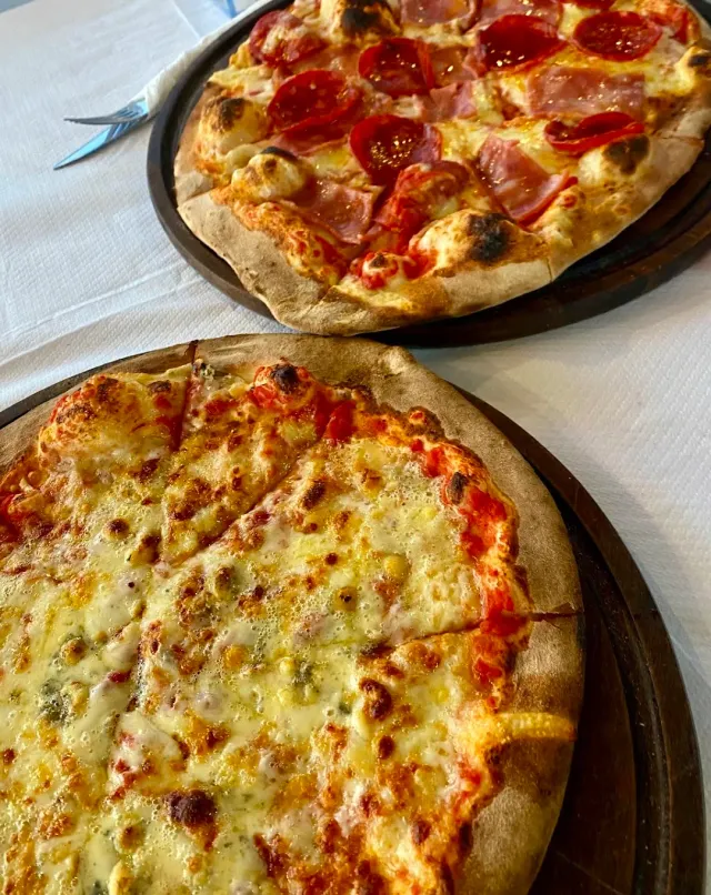 Two pizzas on wooden trays, one with salami and ham and one with cheeses