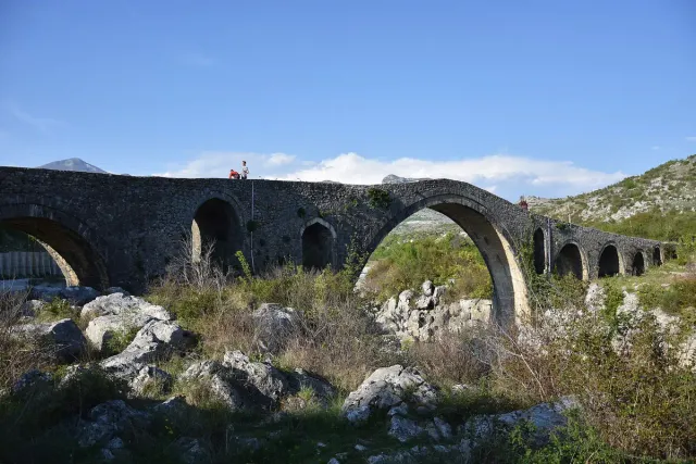A long Ottoman stone bridge with a high central arch over a dry riverbed