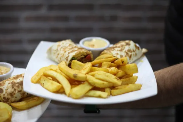 A hand holding a plate with two filled wraps, a pile of fries and a bowl of sauce