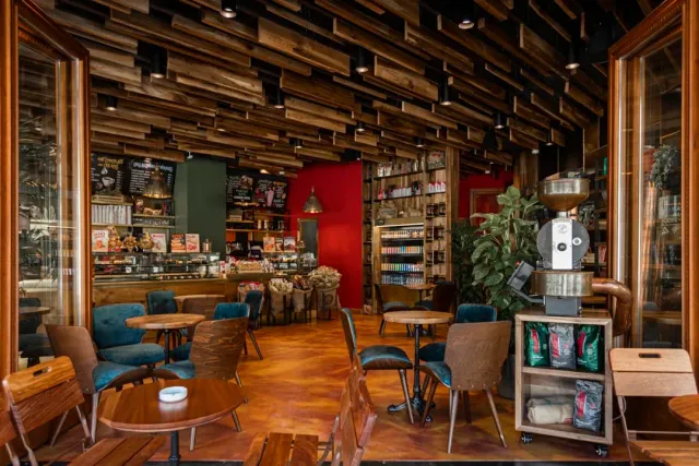 A wide space with a wooden beam ceiling, turquoise armchairs, a red wall and a roasting machine