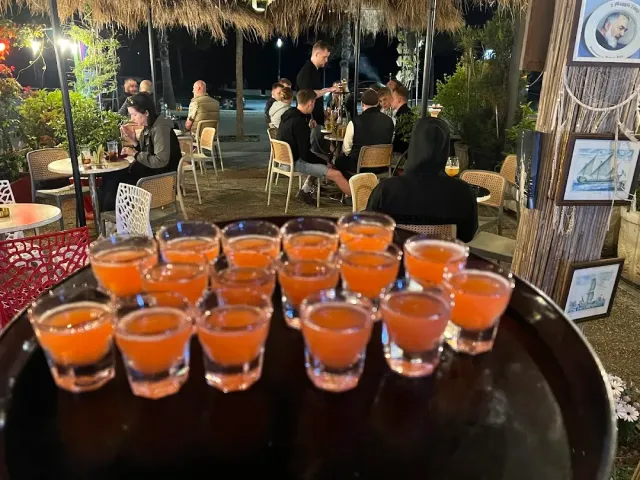 A tray with dozens of orange shot glasses, and behind it people sitting outside at night