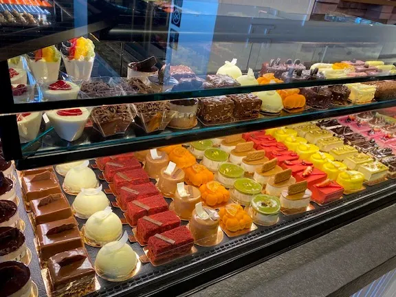 A chilled display case with rows of colorful individual cakes on several shelves