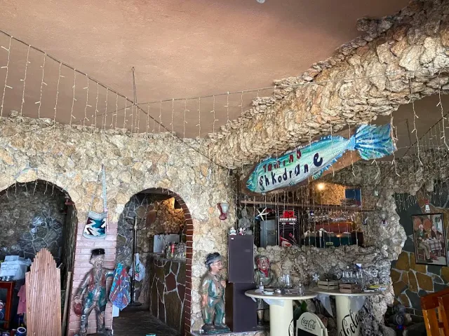 An interior with rough stone walls and arches, a fish shaped sign and figurines on a round table