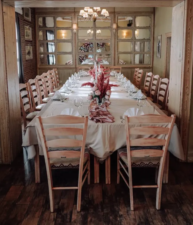 A long table set for a party with a pink flower arrangement and wooden chairs on both sides