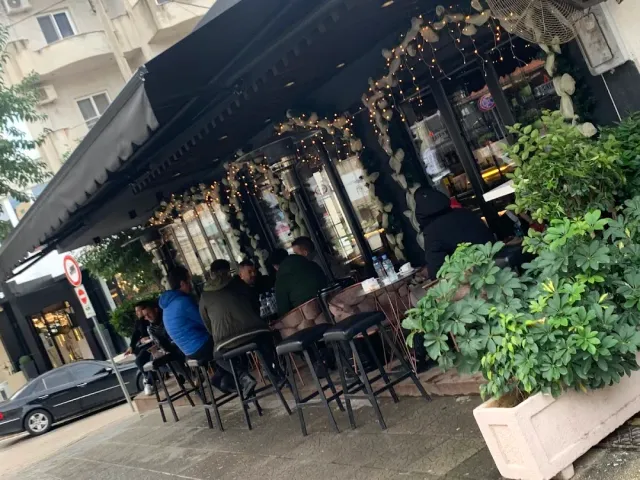 A street terrace under a black awning with string lights and people sitting on high stools