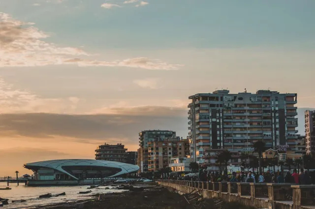 A stone promenade at dusk with tall residential buildings and a rounded structure at the waterline