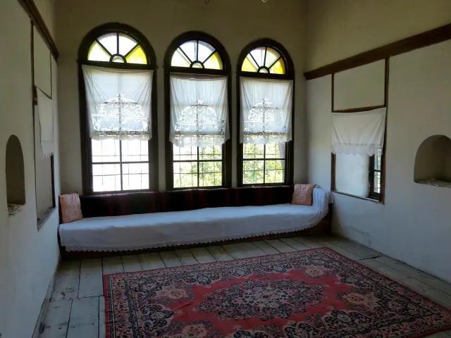 An Ottoman guest room with three arched windows, a low bench along the wall and a red carpet