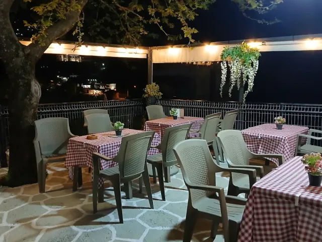 A terrace at night with red checked tablecloths, plastic chairs and a string of lights among the trees