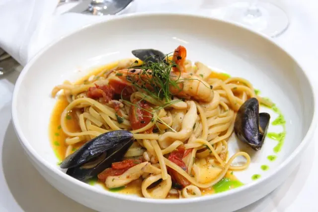 A white bowl with pasta, mussels, shrimp and calamari rings in tomato sauce