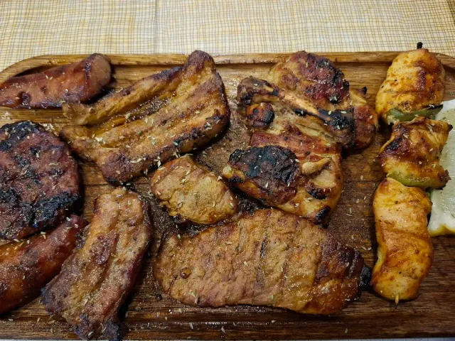 A wooden board loaded with grilled cuts of meat, a patty and chicken skewers