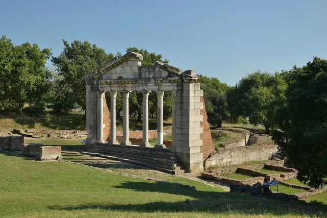 A row of restored Roman columns on a green lawn in an archaeological field