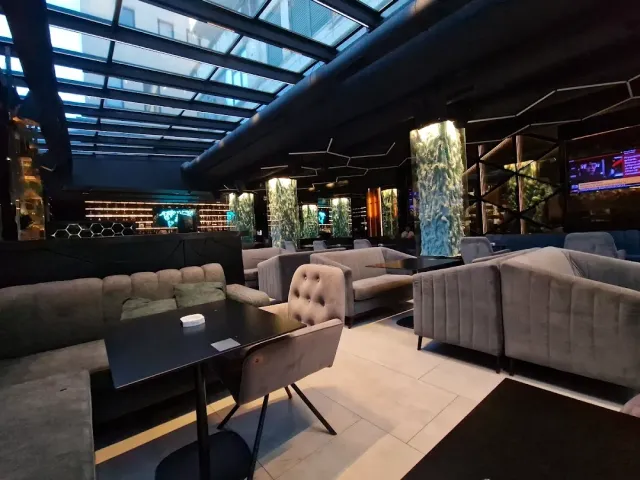 A lounge with a glass ceiling, grey velvet sofas and lit green panels