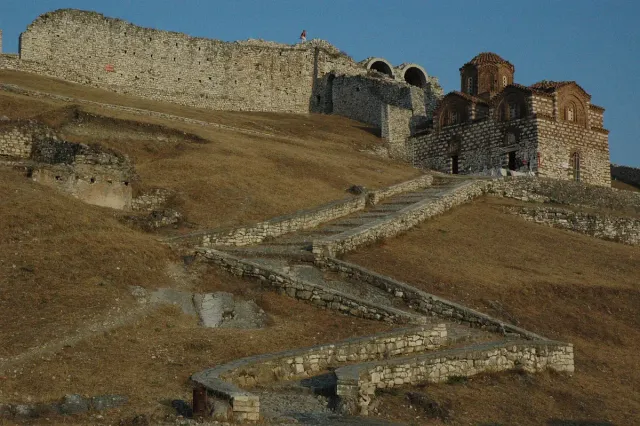 A Byzantine church of brick and stone on a dry hillside below fortress walls