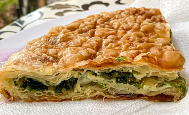 A slice of golden layered pastry filled with spinach and cheese, close up on a napkin