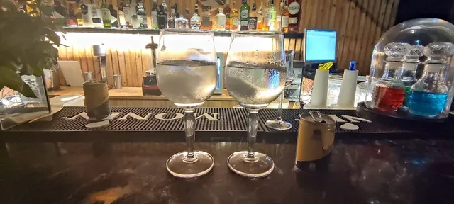 Two glasses of a clear drink on a bar counter, facing lit bottle shelves