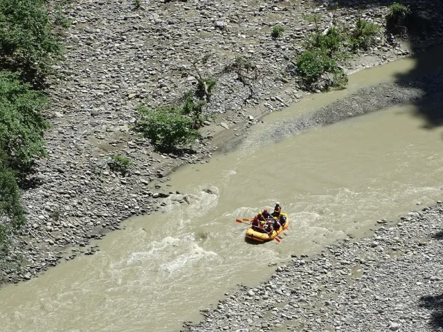 A view from above of a yellow raft with paddlers on a murky river between stony banks