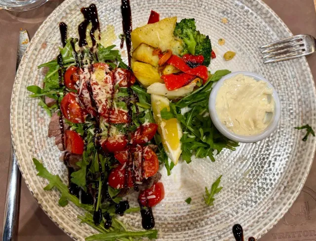 A plate with slices of meat, rocket leaves, cherry tomatoes, grated cheese and balsamic glaze