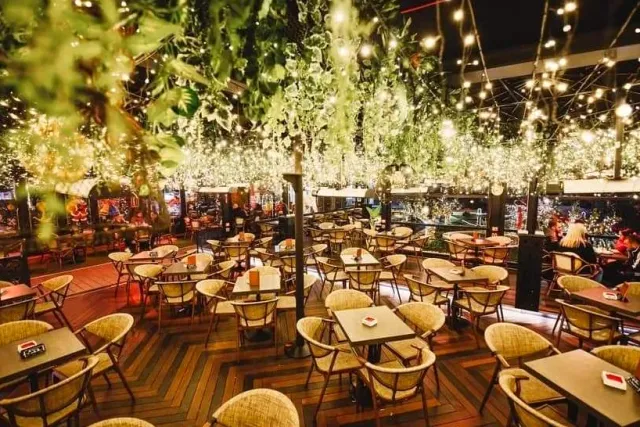 A large hall with hanging greenery, thousands of tiny lights and round tables on a parquet floor