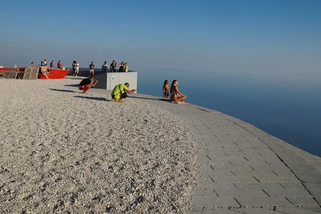 A paved viewing deck ending above the open sea, with visitors standing at its edge