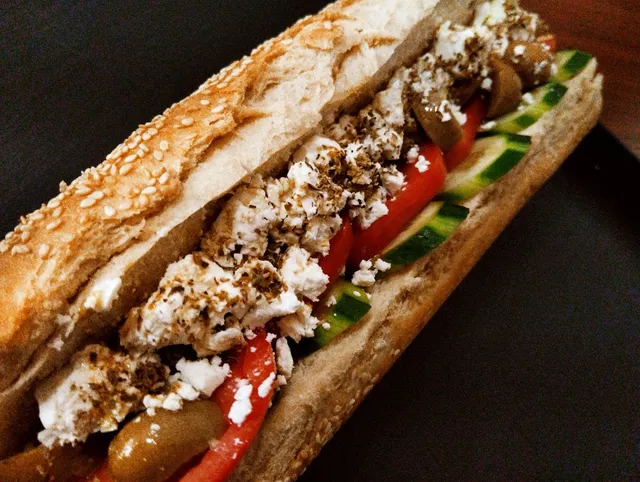 A sesame baguette filled with crumbled white cheese, tomato, cucumber and olives