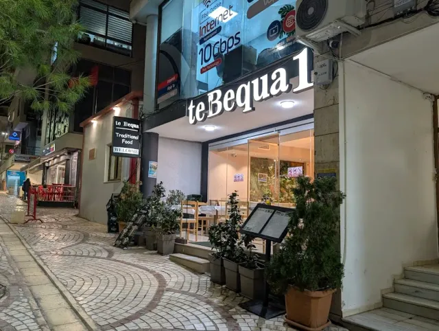 A paved street at night with a lit white sign, pots and a menu board by the entrance