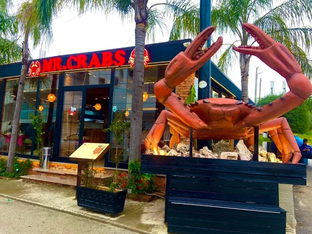A giant crab sculpture at the entrance, a red sign above the glass front and palms on both sides