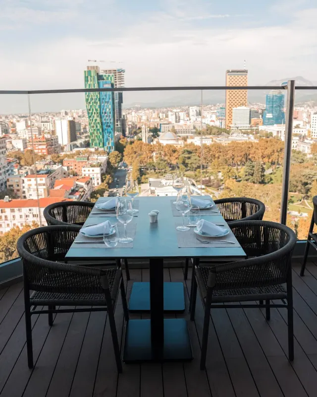 A set table on a glazed rooftop terrace with a panorama of towers and a city