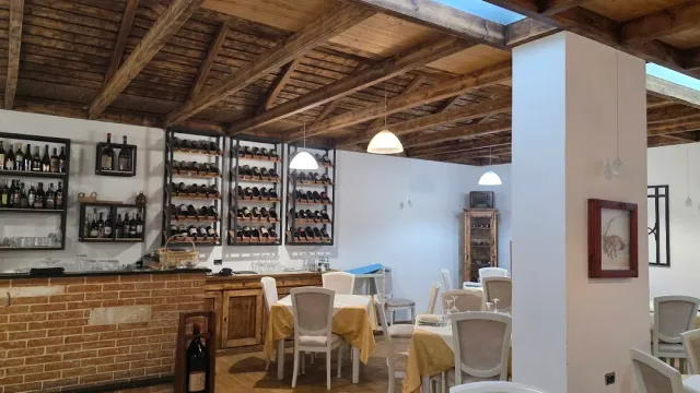 A dining hall with a wooden beamed ceiling, wine racks on the wall and tables with yellow cloths