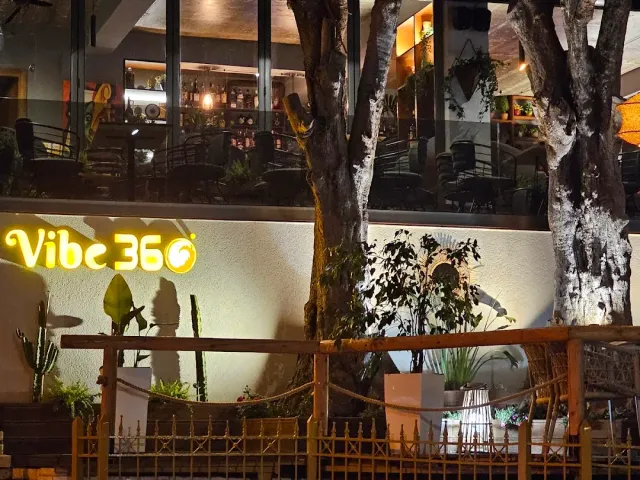 A frontage lit at night with a yellow sign, an upper level behind glass and a wooden fence