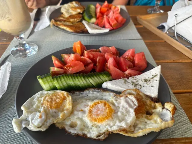 A breakfast of fried eggs, tomatoes, cucumber and white cheese on a wooden table