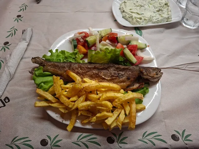 A whole fried trout with fries and vegetable salad on a tablecloth with olive leaves