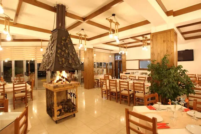 A hall with an open fire under a large metal flue, wooden beams and tables around