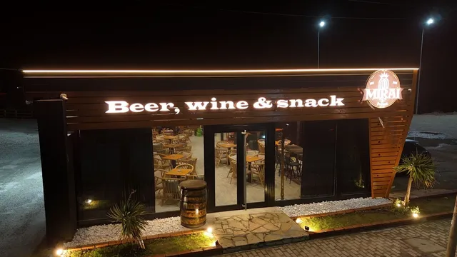 A lit facade at night with an illuminated sign, large glass windows and a wooden barrel at the entrance