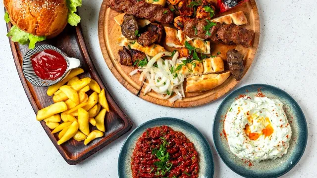 A tray of meat skewers with flatbread and onion, a burger, fries and red and white dips