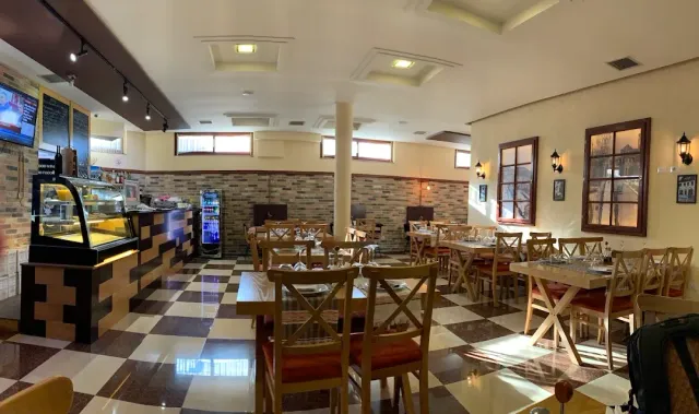A room with a checkered floor, wooden tables and chairs, and a chilled display counter at the side