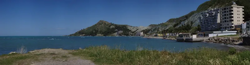 A bay with a green hill and houses on the shore