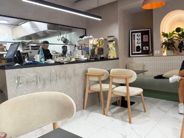 An interior with a counter, an open kitchen behind it and cream upholstered chairs