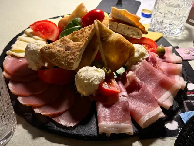 A stone tray with slices of cured meat, cheeses, tomatoes and triangular pastry slices