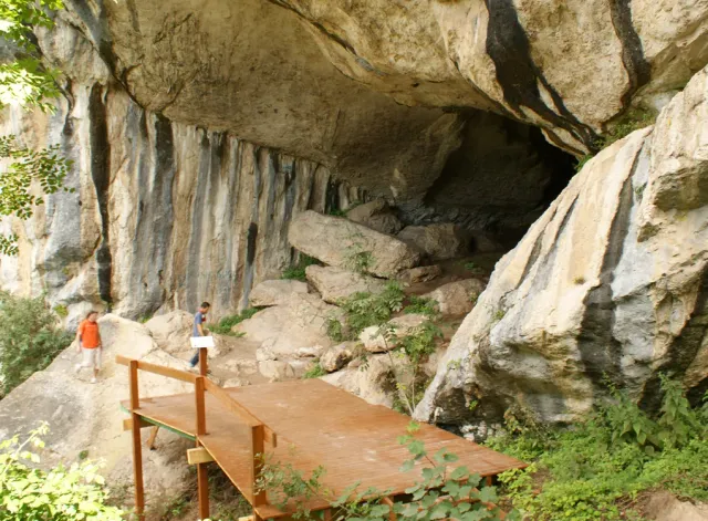 A wide cave mouth in a rock face with wooden steps leading inside