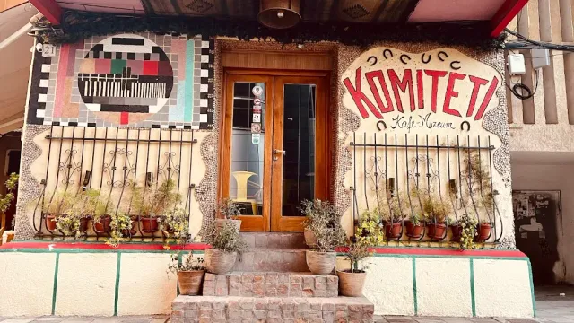 A mosaic decorated facade with painted red letters, a wooden door and pots on the steps
