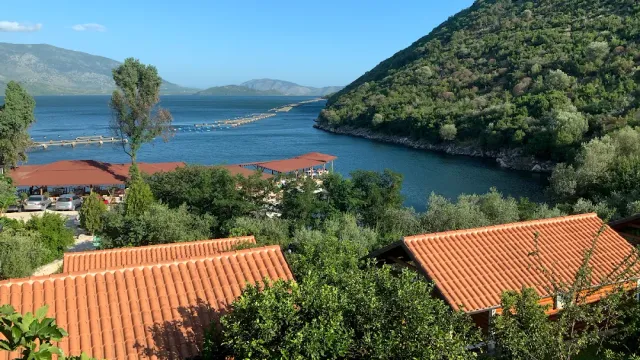 A bay of blue water between green hills, with orange tile roofs in the foreground