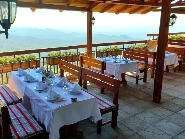 A covered wooden terrace with white clothed tables and benches, facing blue ridges