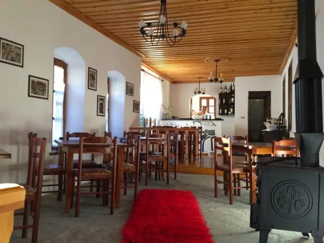 A hall with a wooden ceiling, simple tables and chairs, a red rug and an iron stove