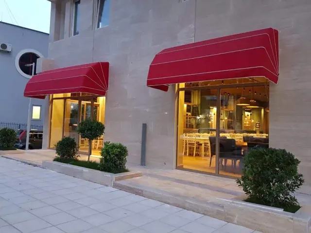 A building front with two red awnings, lit display windows and shrubs in a bed