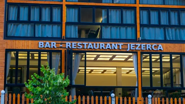 A building front with a blue sign, large windows, light curtains and a wooden fence in front