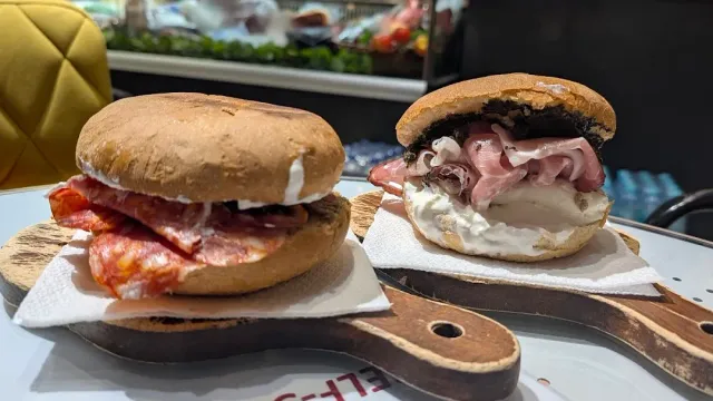 Two open rolls on wooden boards, one with slices of meat and one with cream cheese