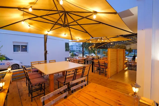 A wooden deck with large yellow umbrellas, hanging bulbs and tables with benches at dusk