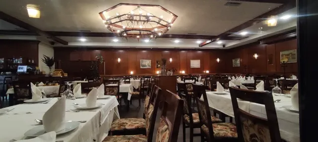 A spacious restaurant hall with white tablecloths, upholstered chairs and a large wooden chandelier on the ceiling