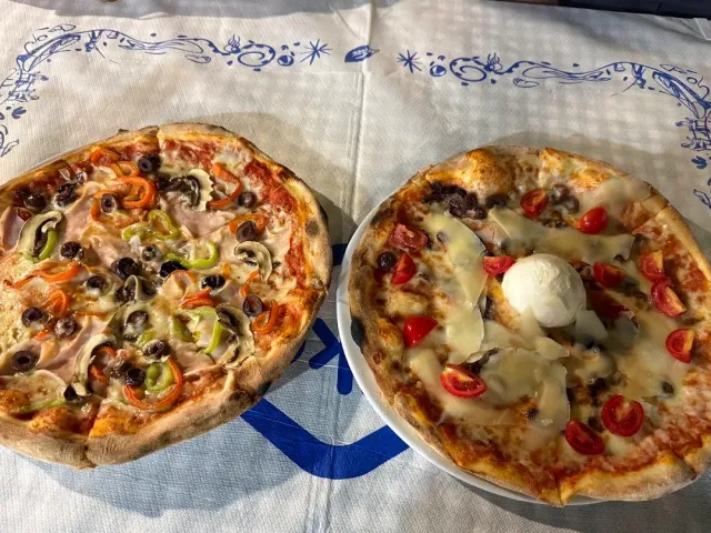 Two pizzas on a white cloth, one with peppers and olives and one with cherry tomatoes